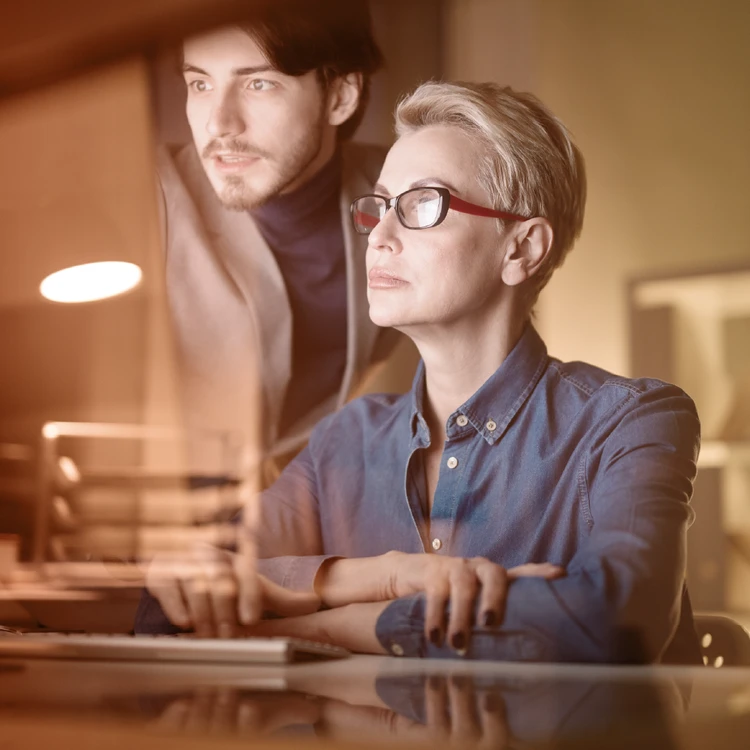 An experienced manager and a young consultant collaborate while analyzing data on a screen, representing corporate values of mentorship, decision-making autonomy, and professional growth.