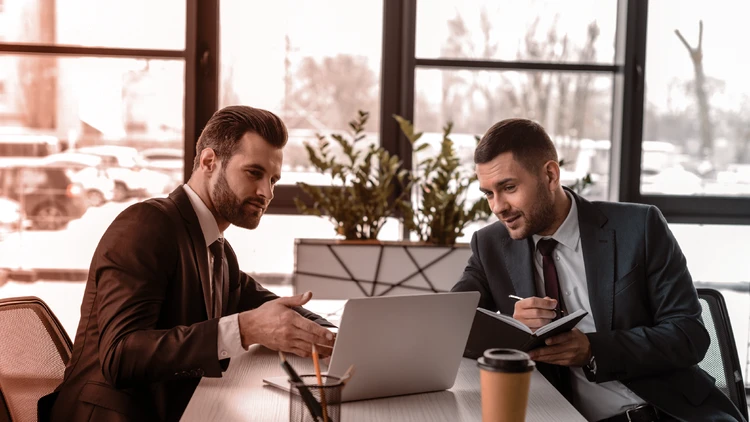Two consultants discuss career opportunities and professional growth pathways in front of a laptop within a bright, modern office.