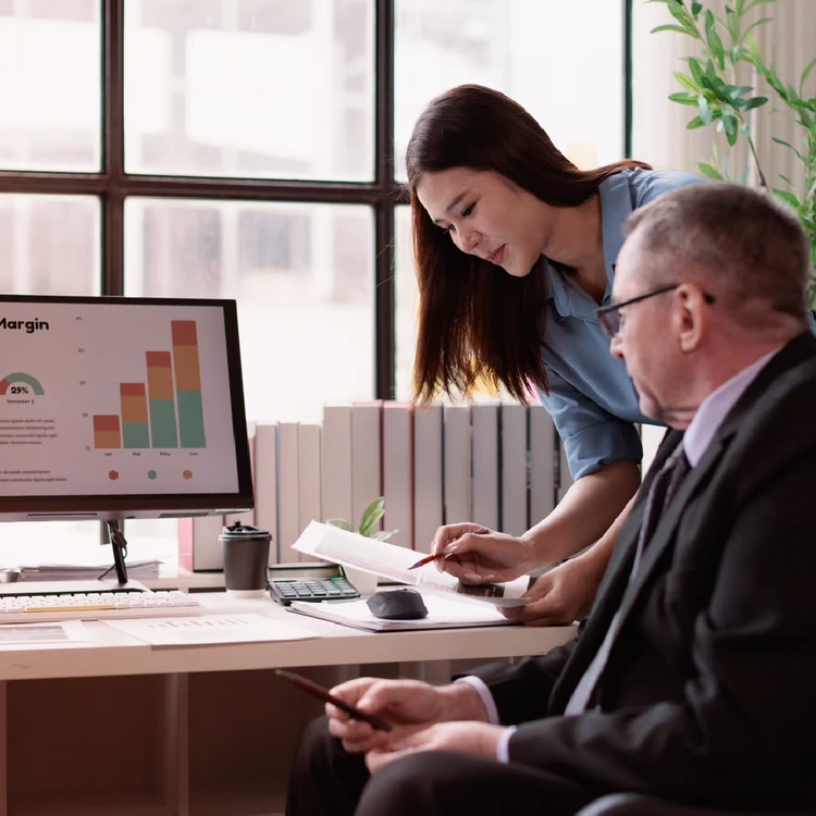 Experts reviewing charts on a computer screen and printed documents in an office, symbolizing verification and accuracy in Data Quality processes.