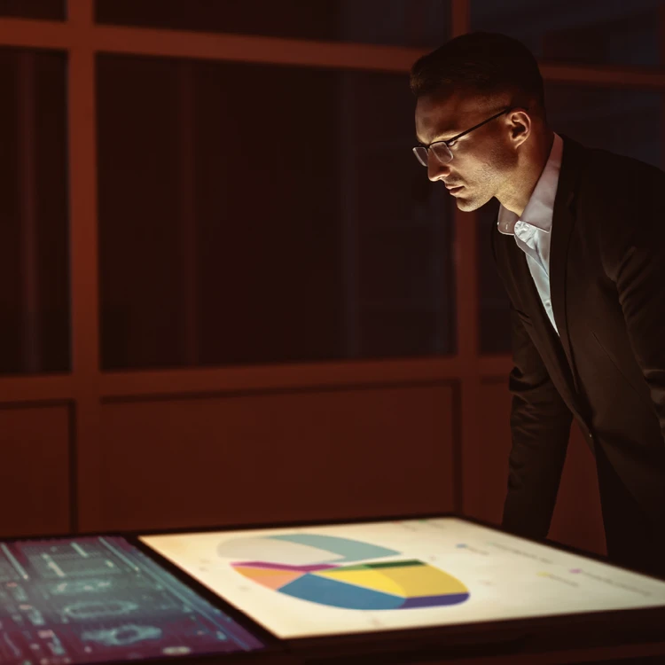 An analyst examines charts and performance metrics displayed on a horizontal touchscreen during a digital innovation and planning session.