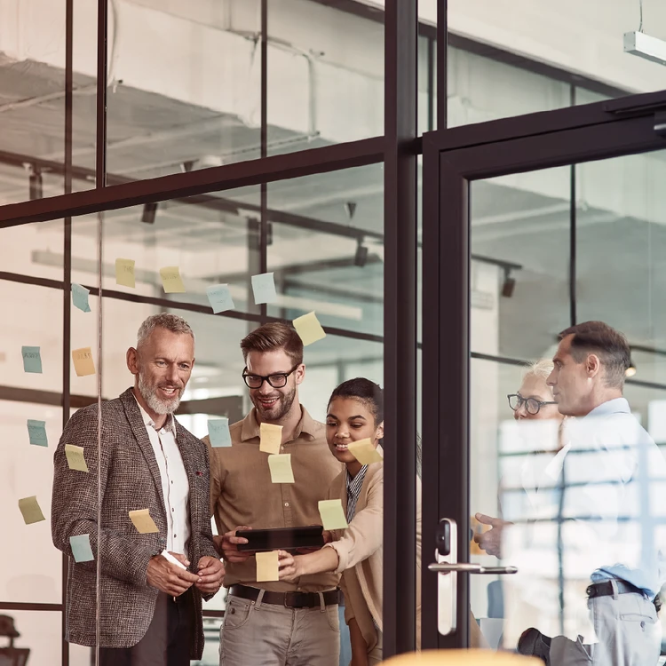 Strategic brainstorming session: a working group plans activities and dynamic business processes using a glass board with sticky notes and a tablet.