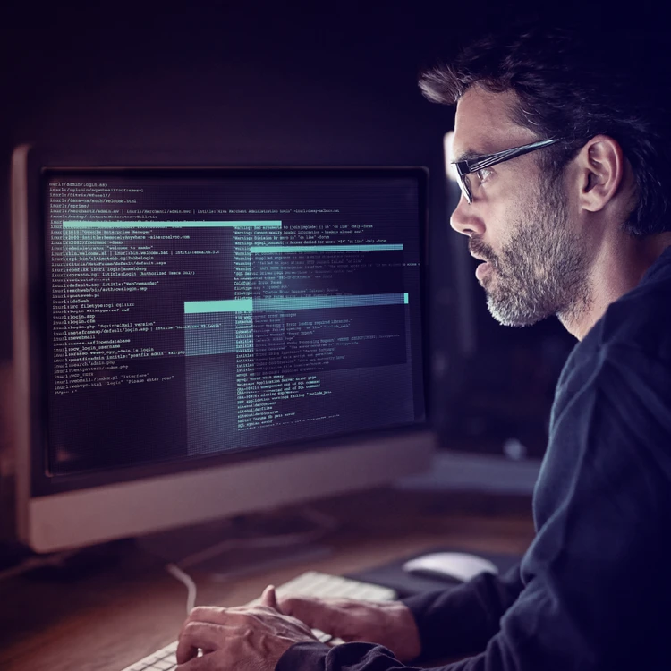 An IT specialist focused on analyzing complex code on a monitor, reflecting strategic IT Advisory and system Architecture re-design.