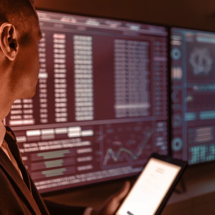 A professional holding a tablet while monitoring interconnected analytics screens, symbolizing data integration in an Omnichannel reboot program.