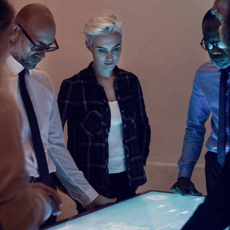 Professionals analyze process flows and complex data on a digital interactive table, collaborating on a client's operating model transformation.