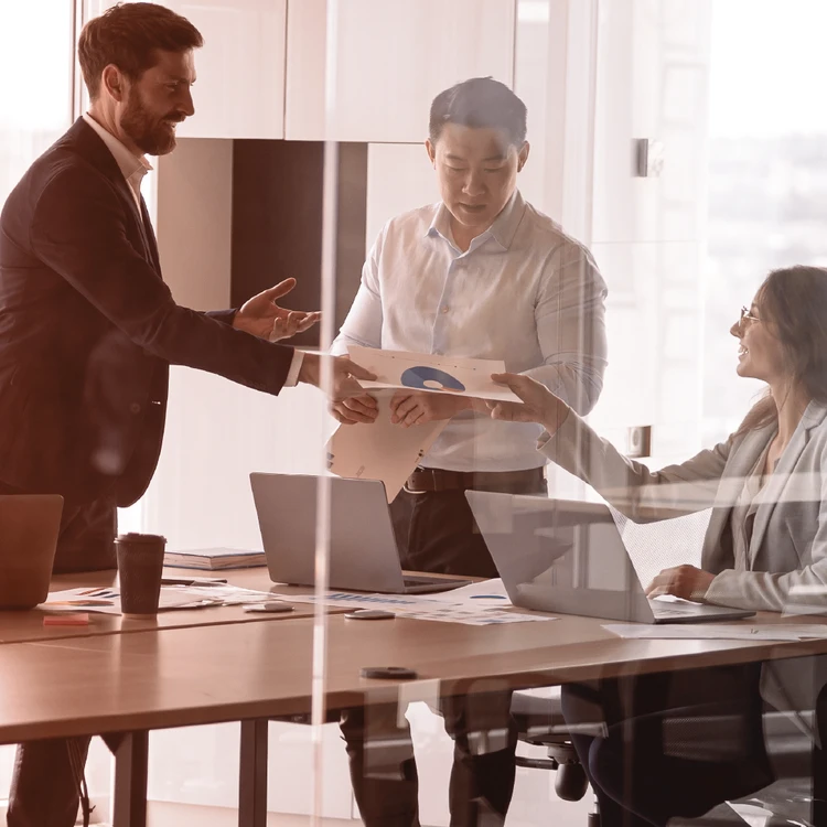 Three management consultants actively collaborate in an office, exchanging reports and charts to optimize the client's operating model and strategic execution.