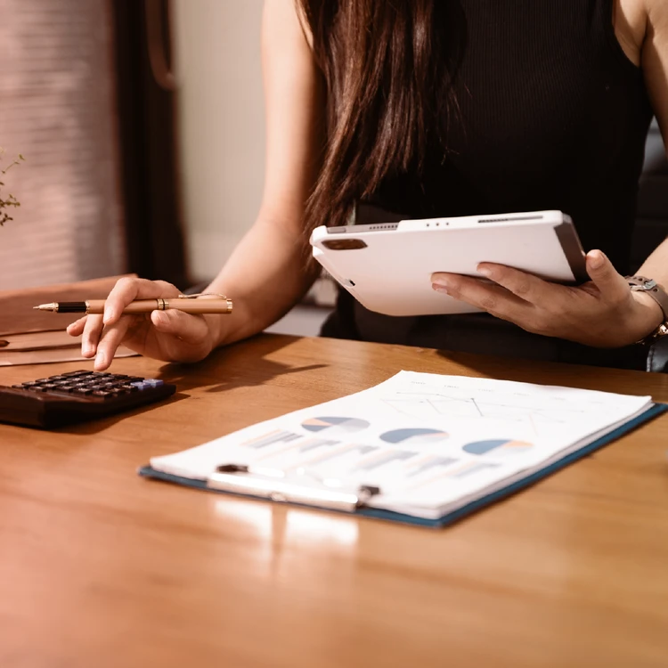 A person analyzing financial documents and charts at a desk using a tablet and a calculator, symbolizing the fast and efficient management of personal & consumer fast finance services.
