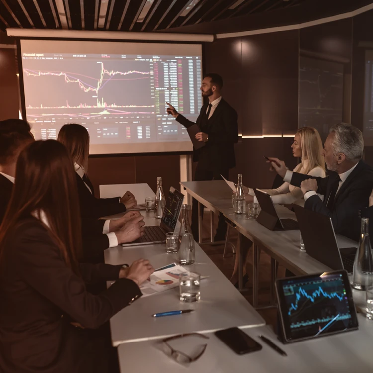 A team collaborates to examine dynamic financial charts projected on a large screen and displayed on mobile devices, guiding business decisions towards the desired impact.