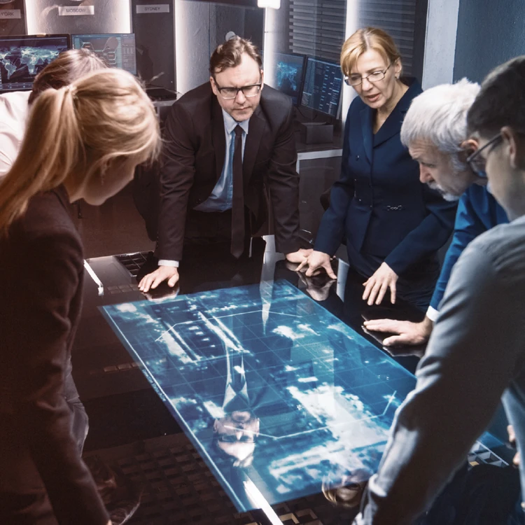 A team of management consultants and executives analyze development plans on a digital interactive table, collaborating to define business design and strategy.