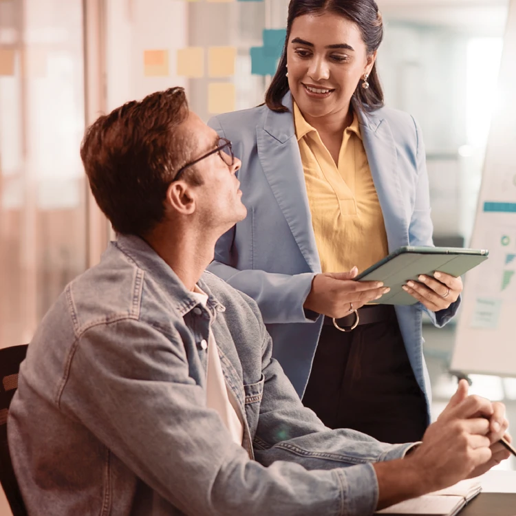 Two professionals collaborate in an agile workspace, sharing data on a tablet to promote Teal organizational models based on self-management and cooperation.