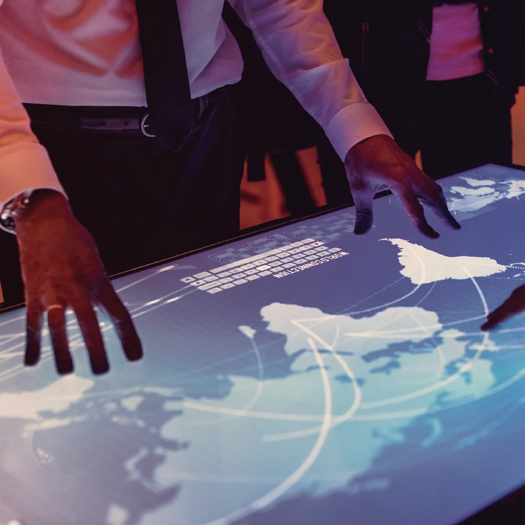 Professionals interact with a global map on an interactive touch-screen display, representing the intersection of business strategy and advanced digital technology.
