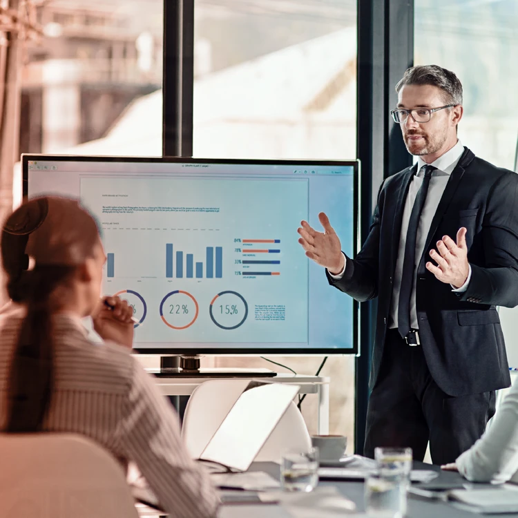 Business presentation in front of a large digital screen showing charts, percentages, and performance metrics, illustrating strengths and competitive advantages for clients.